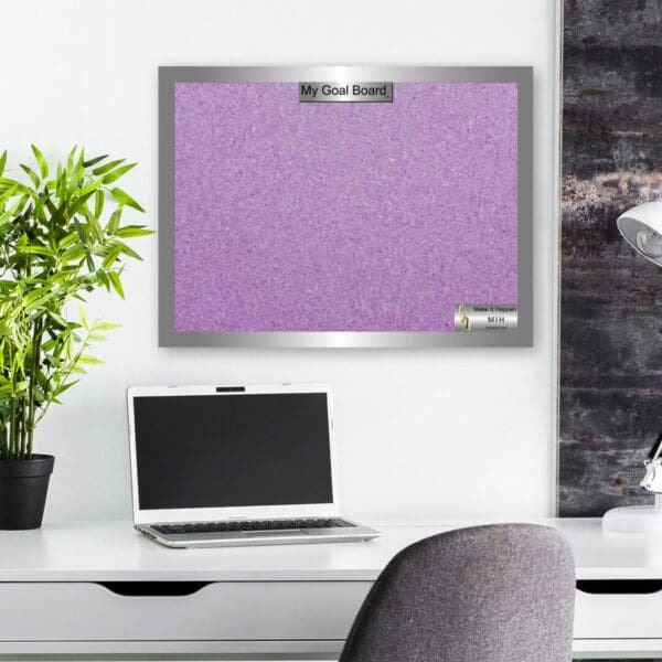 A laptop and plant on a desk with a purple bulletin board.