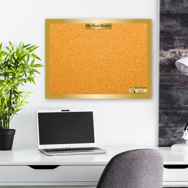 A laptop and plant on a desk in front of a cork board.