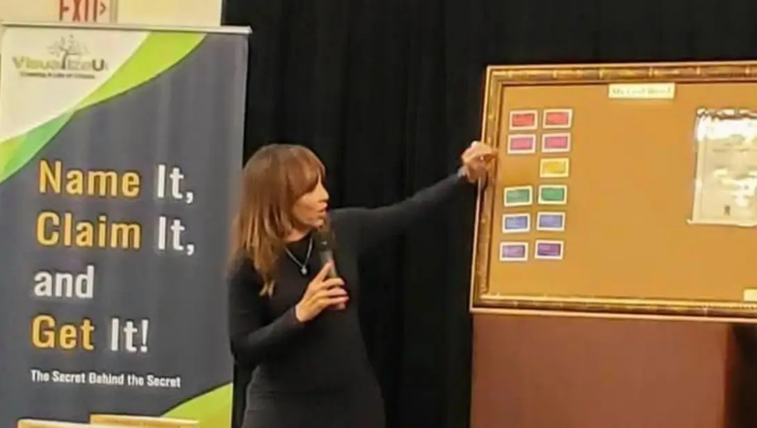 A woman pointing to a board with many different colored magnets.