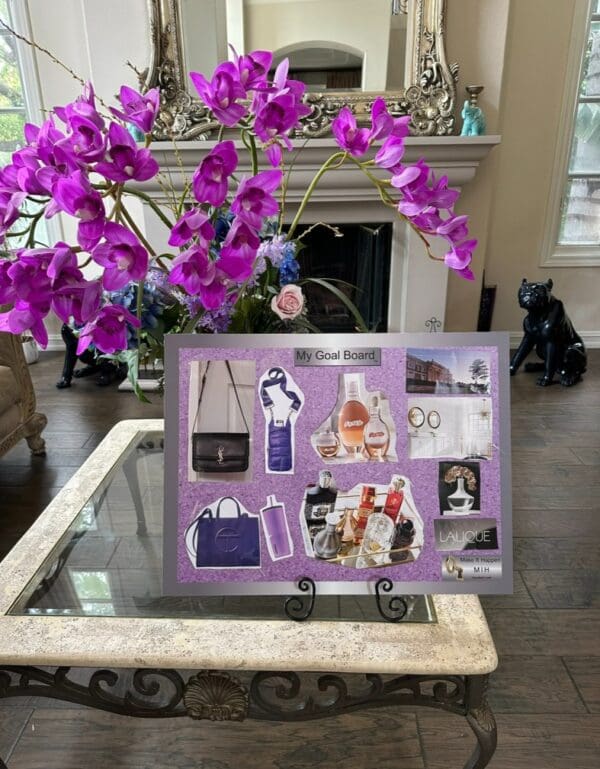 A 15 inch Metal Easel Stand featuring images of luxury items including bags and perfumes, displayed on a glass table with purple orchids and a mirror in the background.
